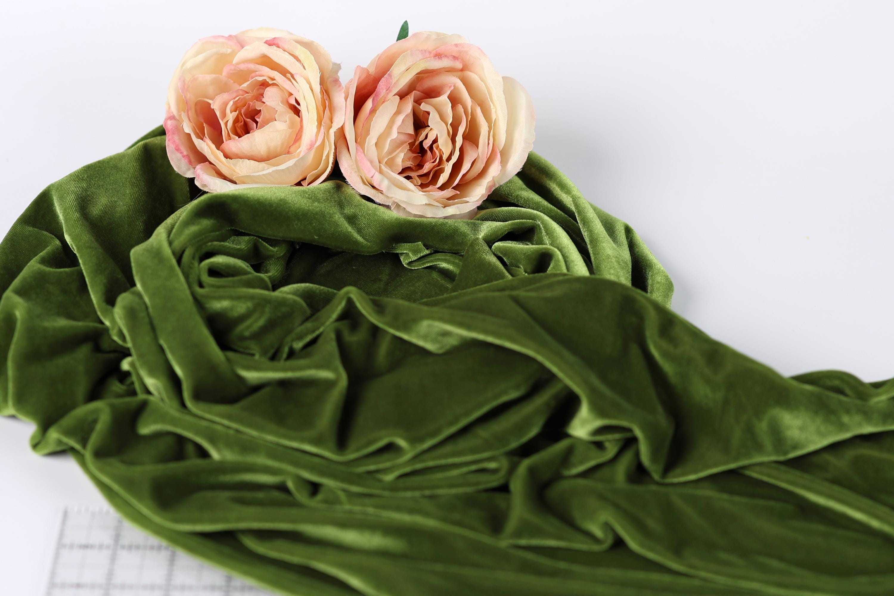 two pink roses resting on a crumpled green fabric.