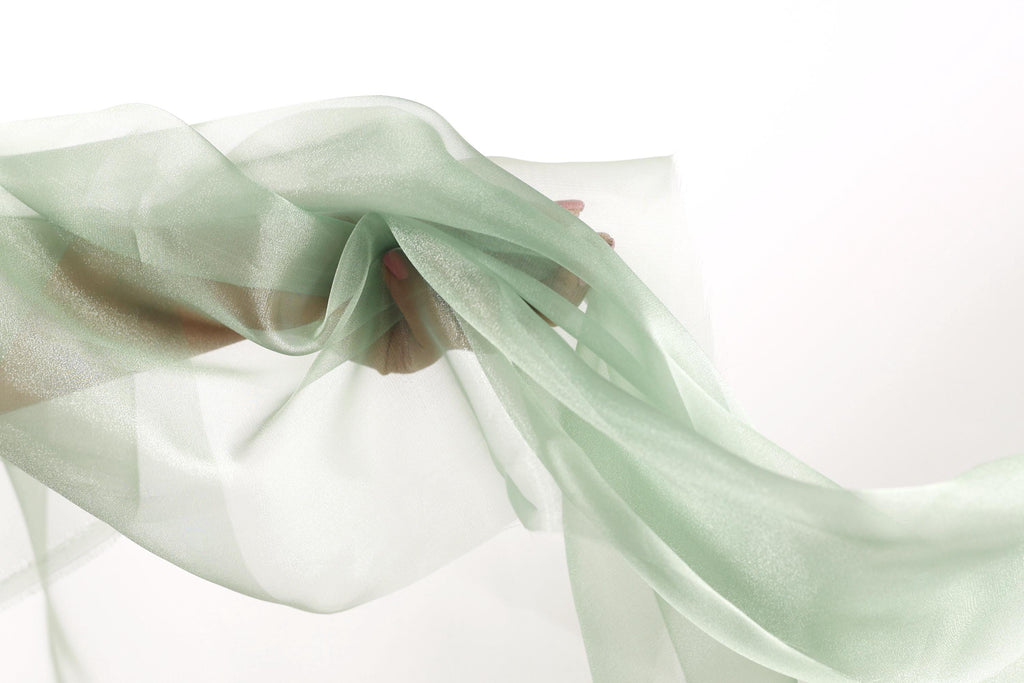 A hand is holding a piece of green fabric, which appears to be flowing or billowing in the air.