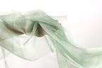 A hand is holding a piece of green fabric, which appears to be flowing or billowing in the air.
