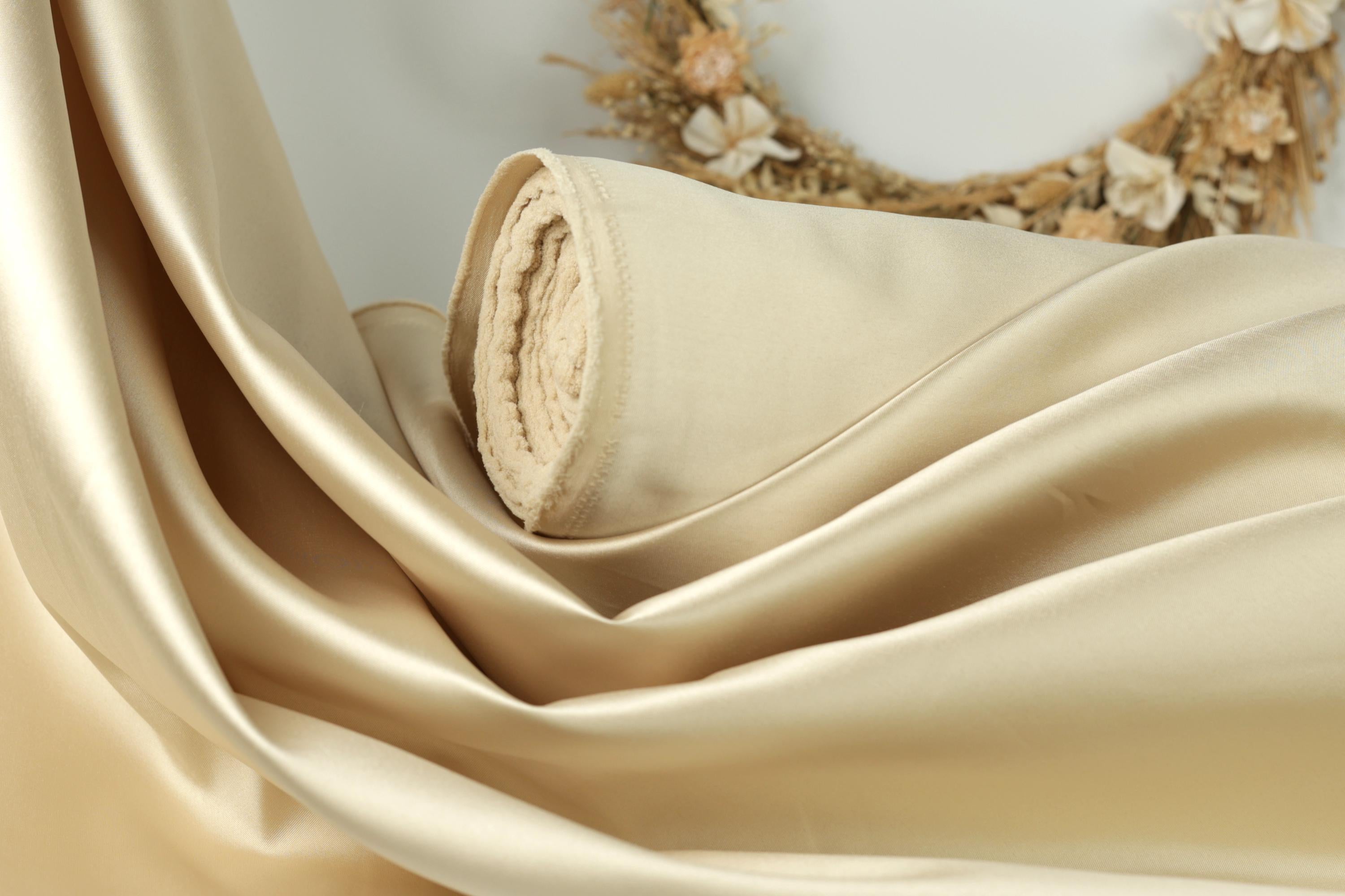 A close-up view of a piece of light-colored fabric, possibly silk or satin, with a wreath of dried flowers in the background.