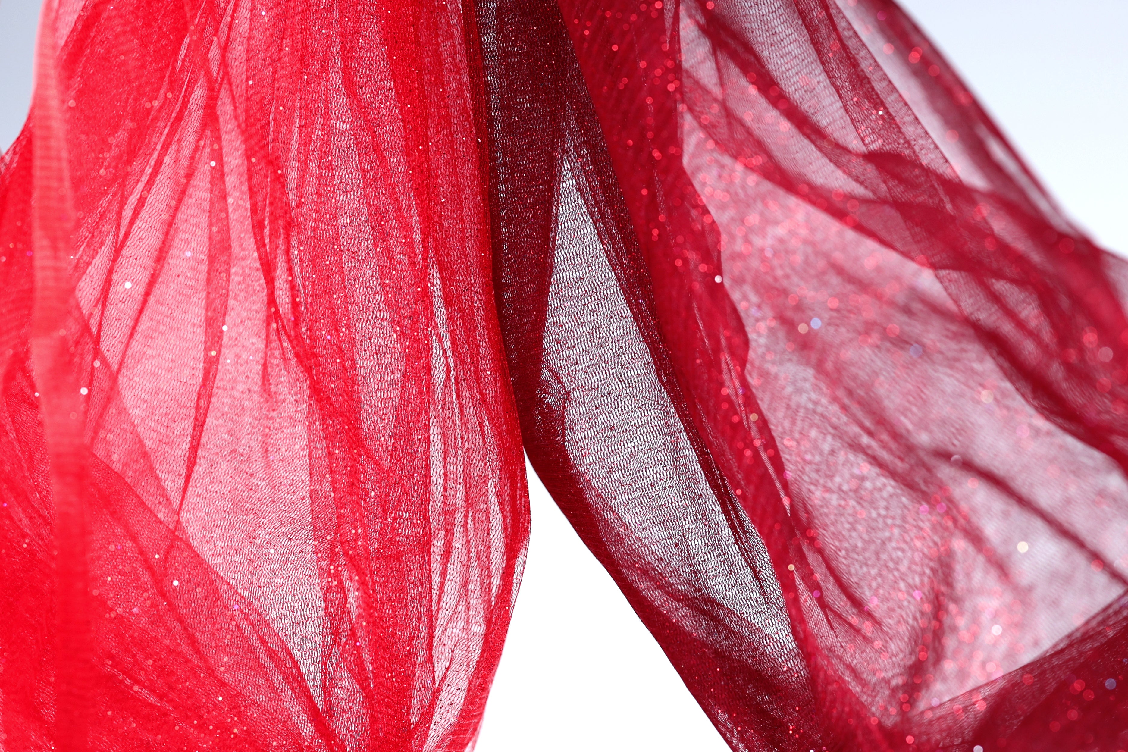a close-up view of a red fabric, possibly a sheer or sheer-like material, with a textured and flowing appearance. The fabric appears to be made of a sheer or sheer-like material, which is characterized by its delicate and transparent nature. The fabric is slightly wrinkled, adding to its overall texture and visual appeal.