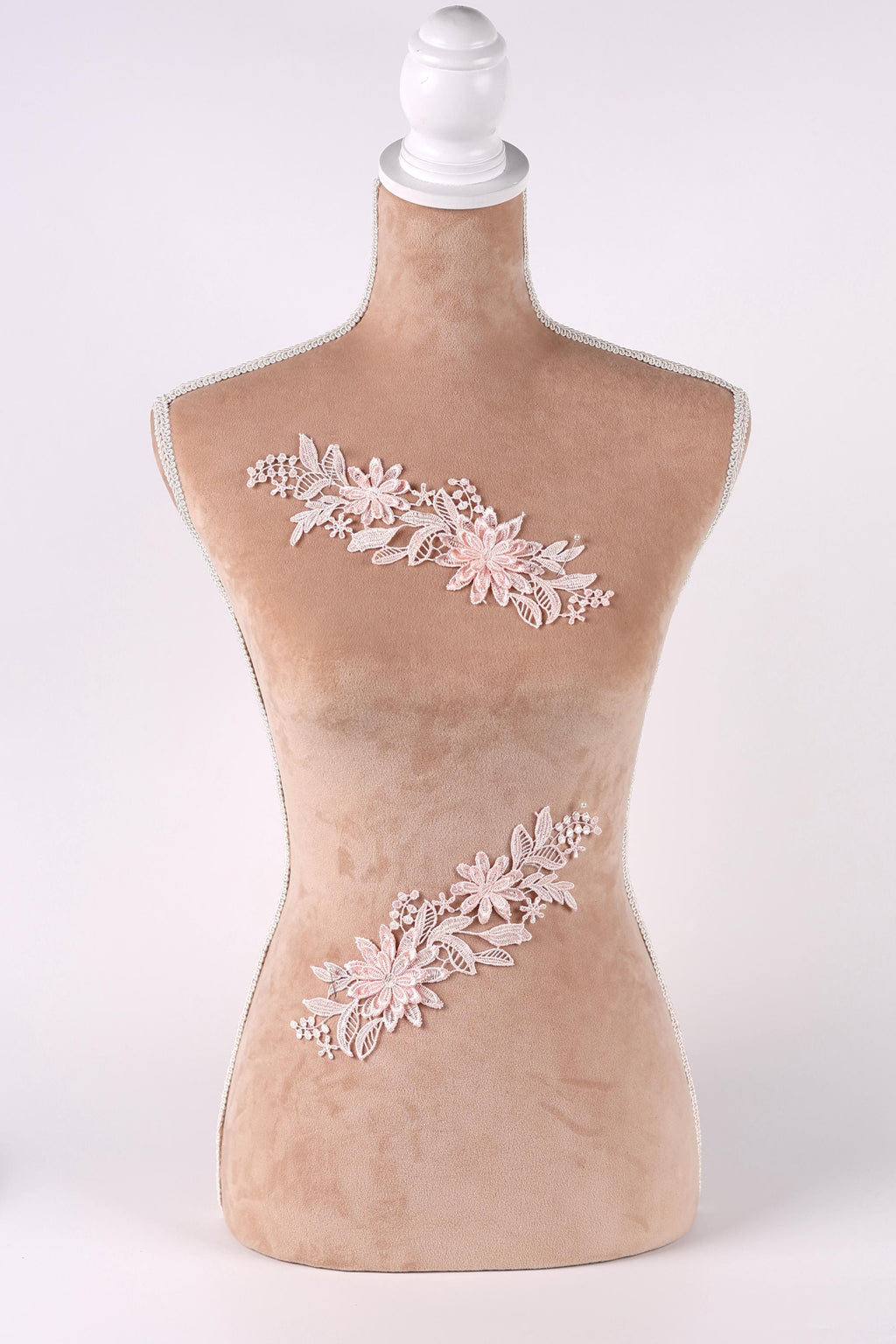 A mannequin with a beige body and a white head, wearing a floral embroidered piece of clothing.