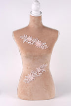 A mannequin with a beige body and a white head, wearing a floral embroidered piece of clothing.