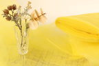 a clear glass vase filled with flowers and a yellow fabric or material, placed on a yellow background.