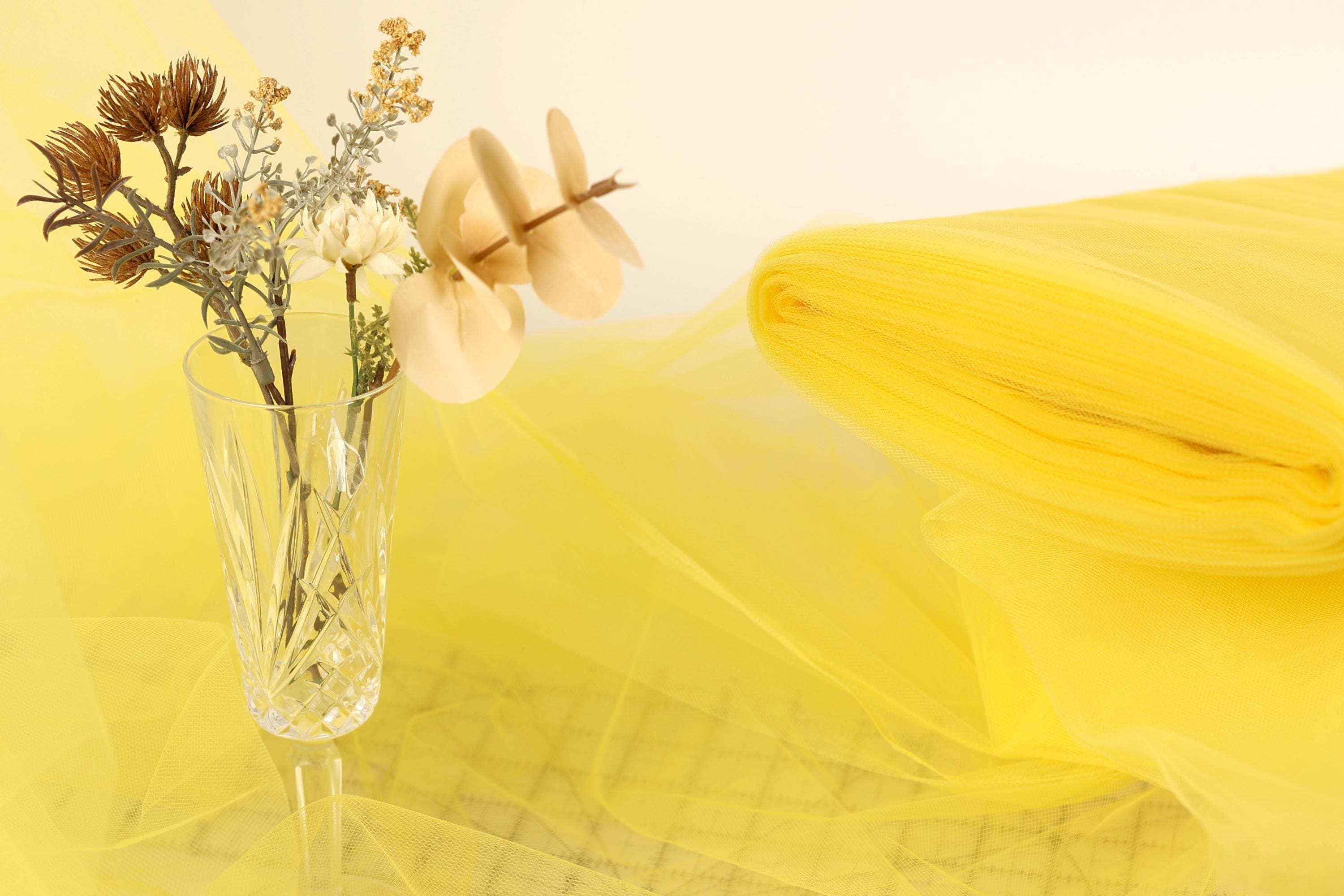 a clear glass vase filled with flowers and a yellow fabric or material, placed on a yellow background.