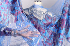 A hand is holding a piece of fabric with a blue and purple patterned design, which appears to be a decorative textile or garment.