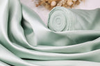 A close-up view of a light green satin fabric, possibly silk, with a rolled-up end visible.