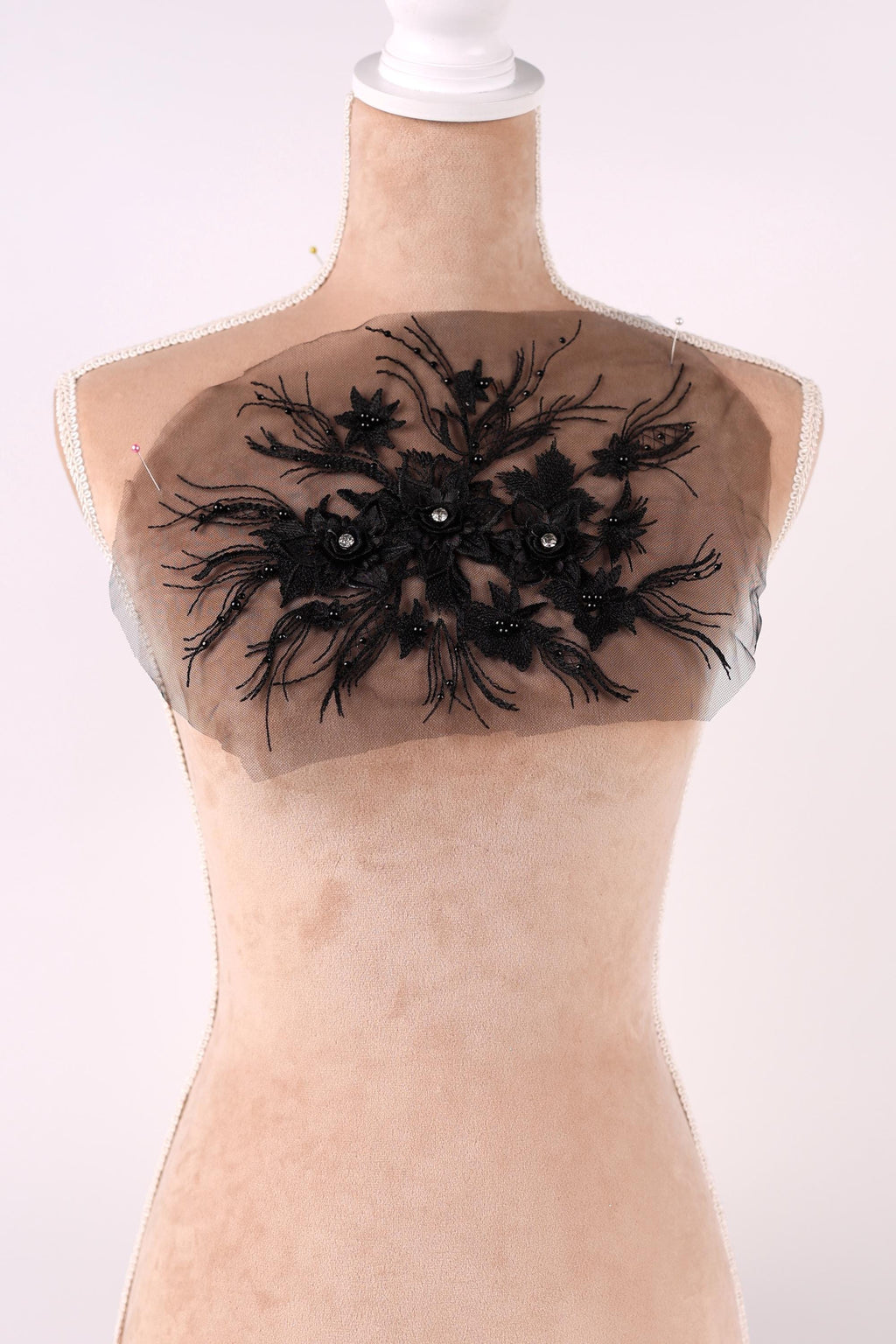 A mannequin wearing a dress with a black floral embroidered patch on the chest area.