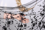 A hand is holding a black fabric with a floral pattern, partially obscuring the view of the background.