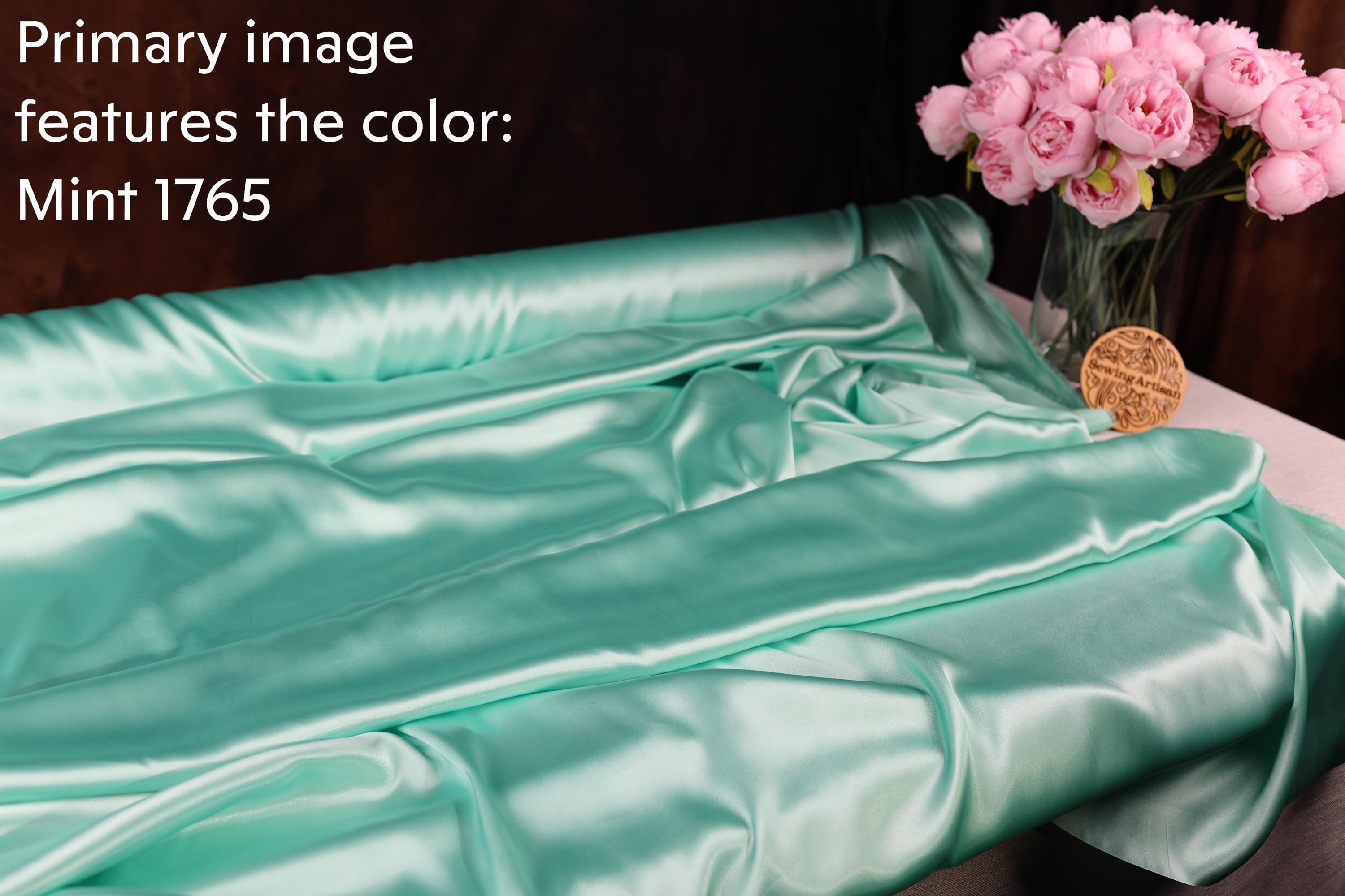 a mint green satin fabric draped over a table, with a vase of pink roses placed next to it.