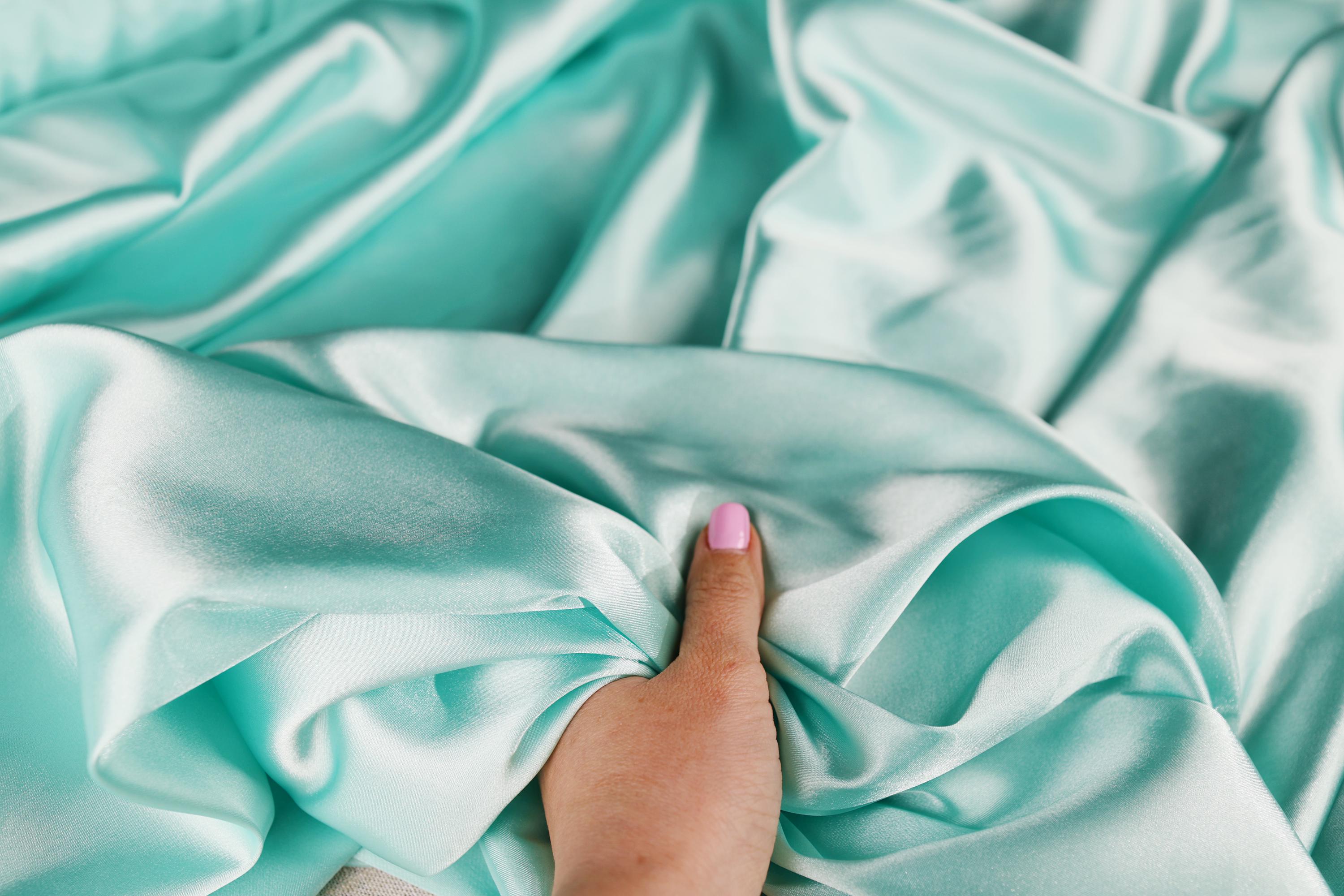 a person&#39;s hand on a blue satin sheet