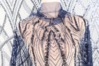 a mannequin wearing a dress with a sheer, sequined bodice and sleeves. The dress has a pattern of blue and black sequins, creating a visually striking and elegant design.