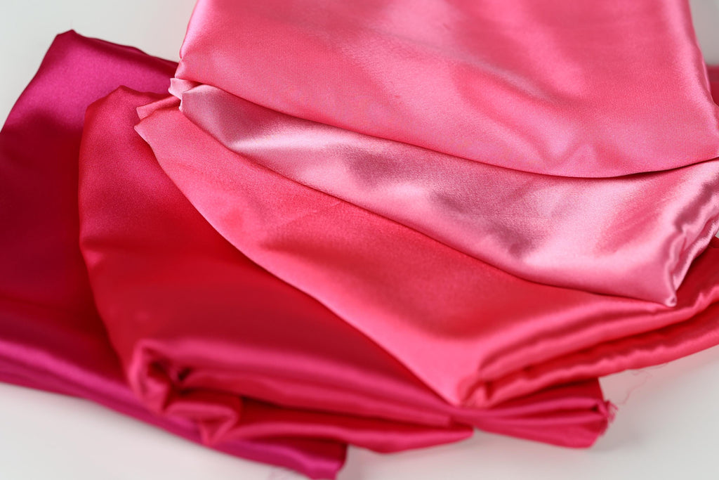 a close-up view of several pieces of pink satin fabric, with varying degrees of wrinkled texture.