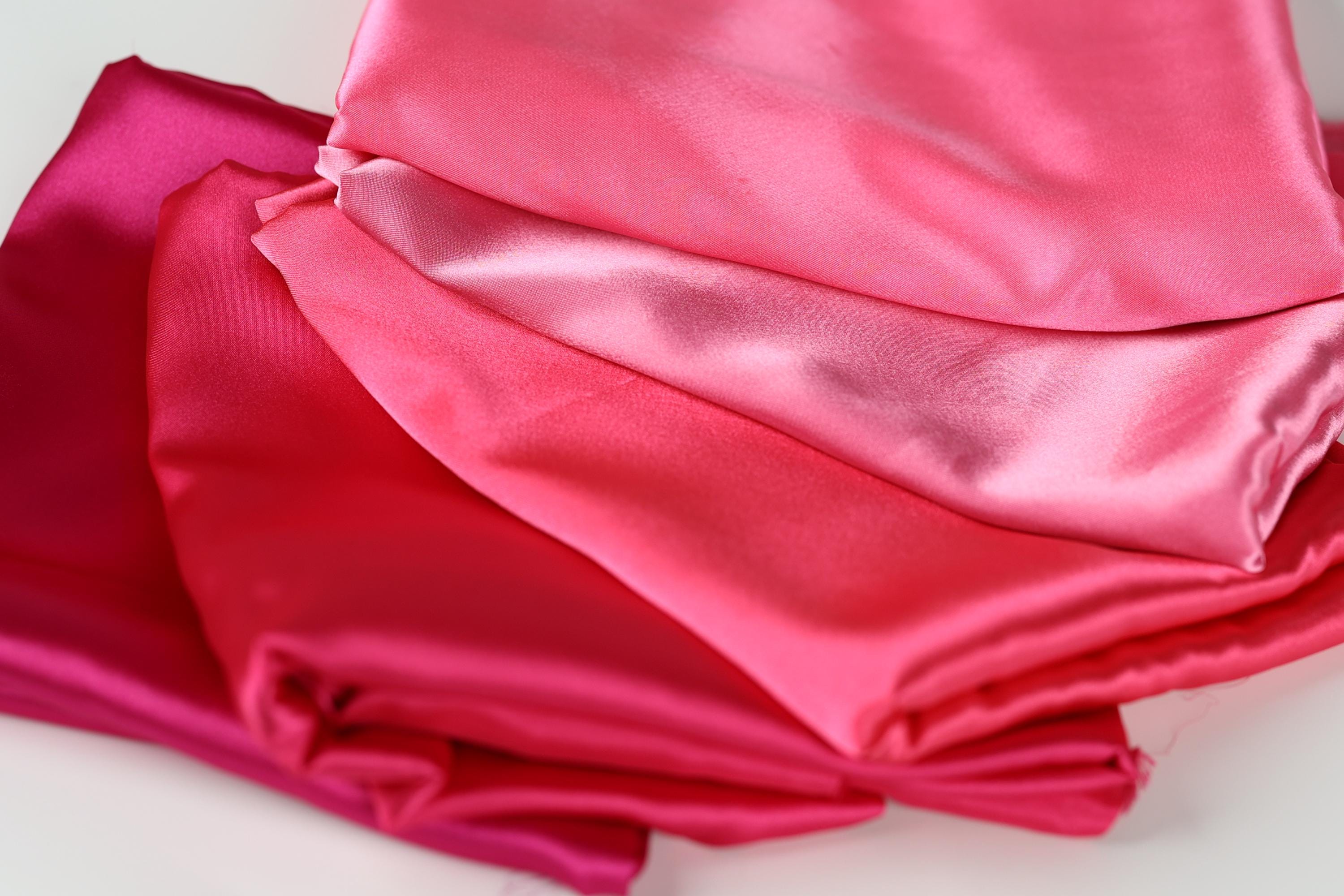 a close-up view of several pieces of pink satin fabric, with varying degrees of wrinkled texture.