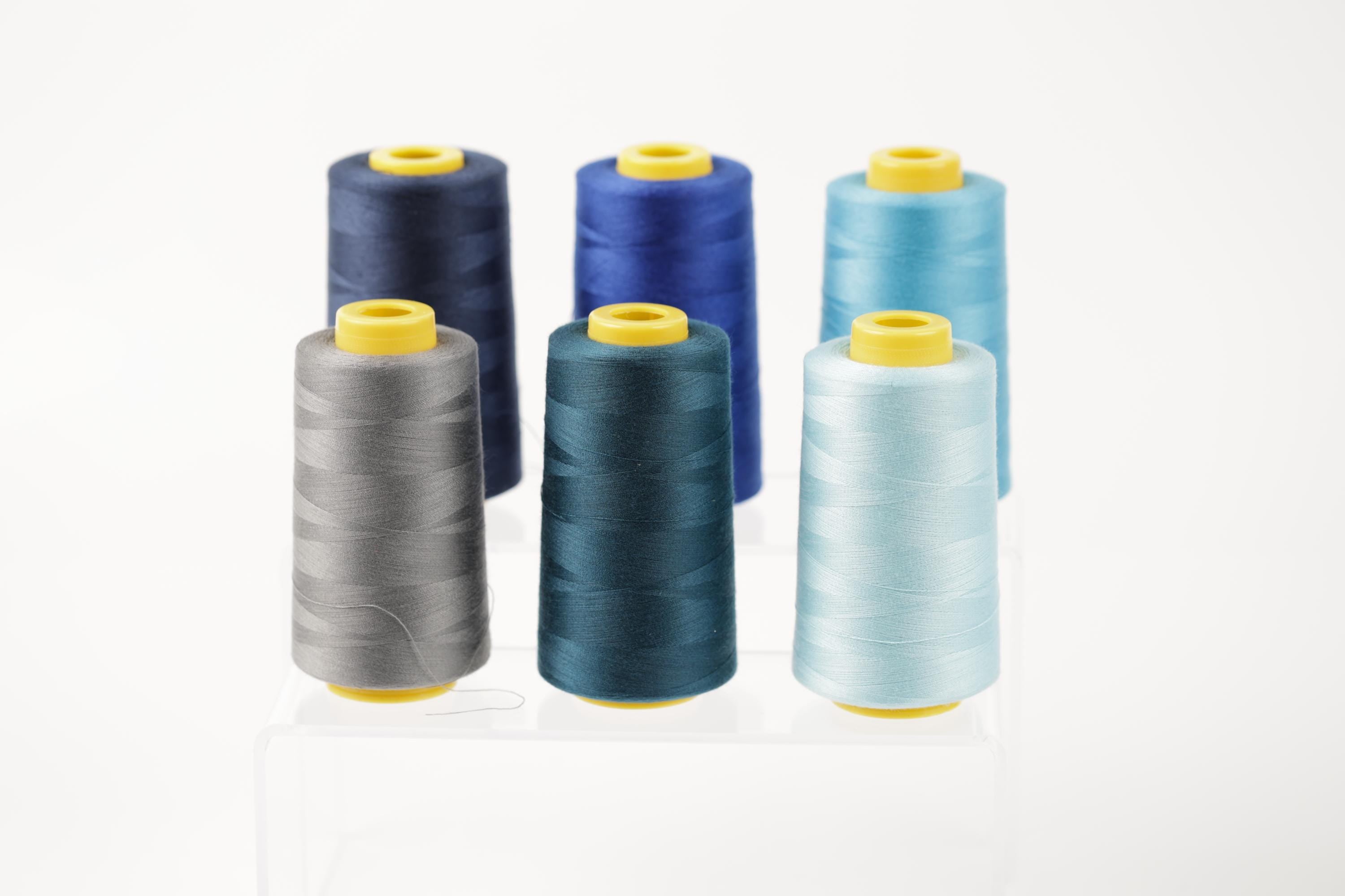 six spools of thread in various colors, including blue, gray, and light blue, arranged in a row.