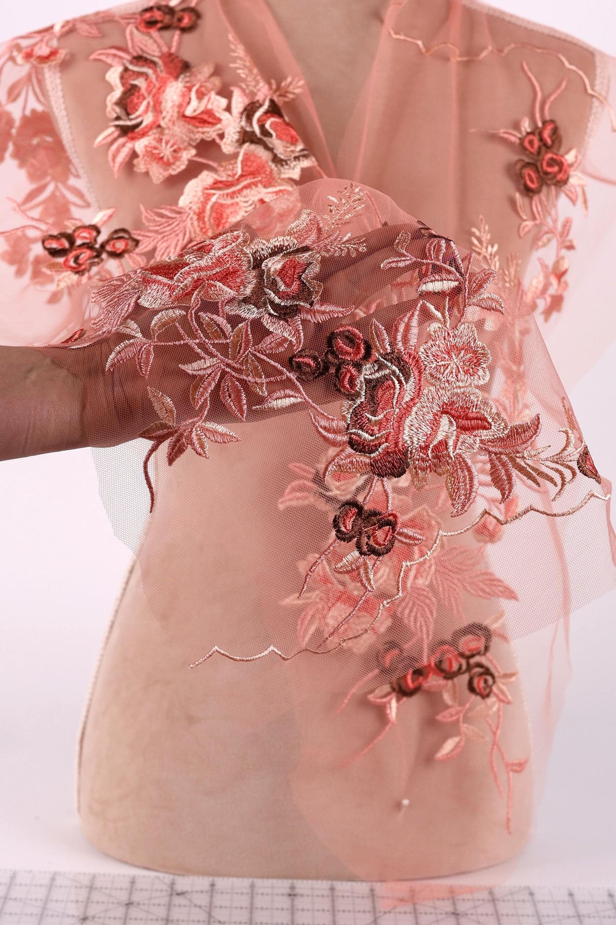 a mannequin wearing a pink dress with intricate floral embroidery. The dress is displayed on a mannequin, showcasing the detailed and colorful design.