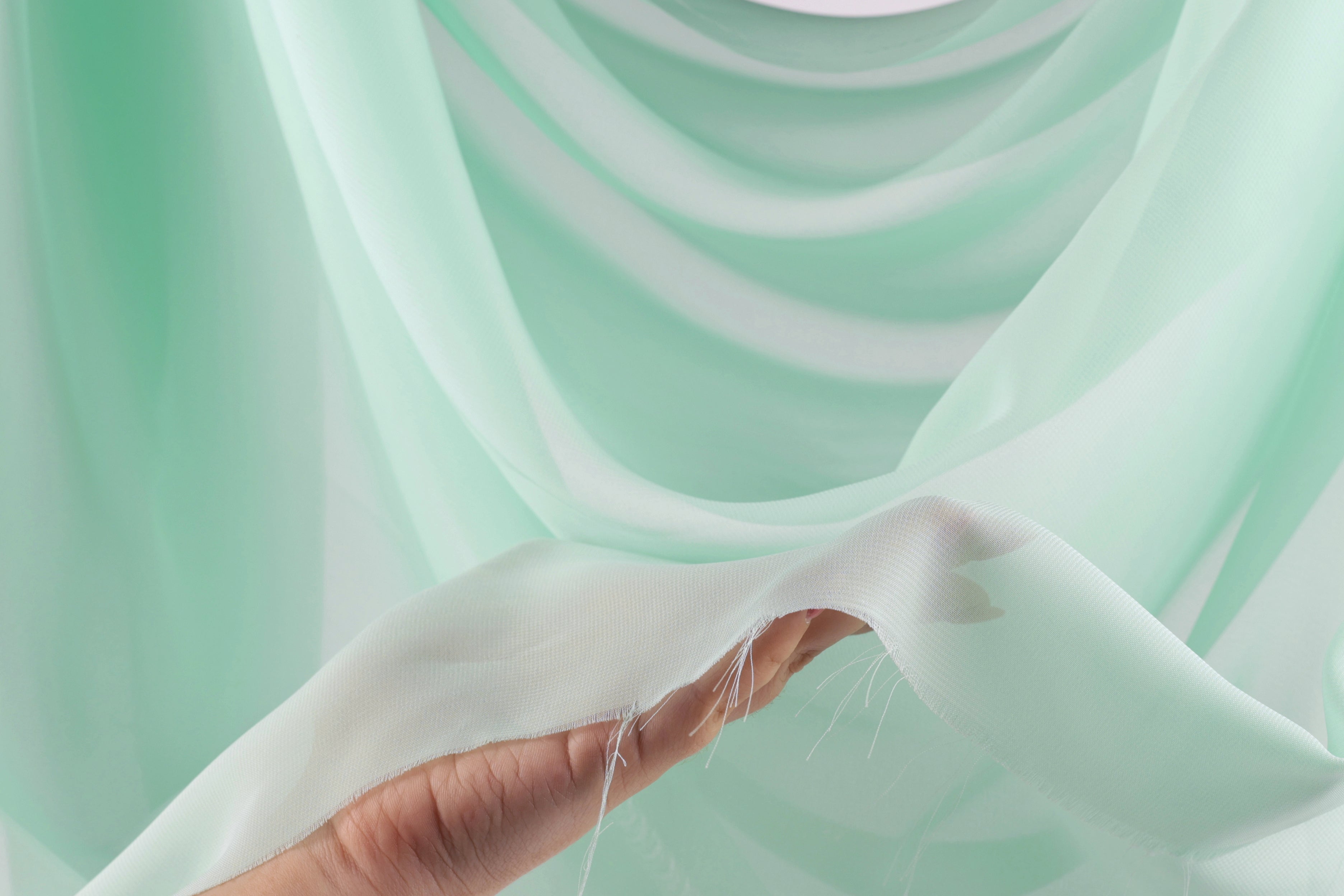 A hand holding a piece of white fabric with a green background.