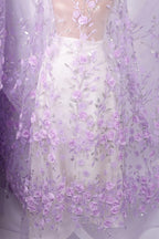 a white dress with a sheer, floral-patterned fabric draped over it. The fabric is adorned with numerous small, delicate purple flowers, creating a visually striking and elegant appearance.