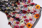 a close-up view of a fabric with a vibrant floral pattern. The fabric is adorned with a variety of colorful flowers, including red, orange, yellow, and purple flowers, creating a visually striking and intricate design. The fabric appears to be a lace-like material, with the flowers intricately embroidered or sewn onto it, adding a touch of elegance and sophistication to the overall appearance.