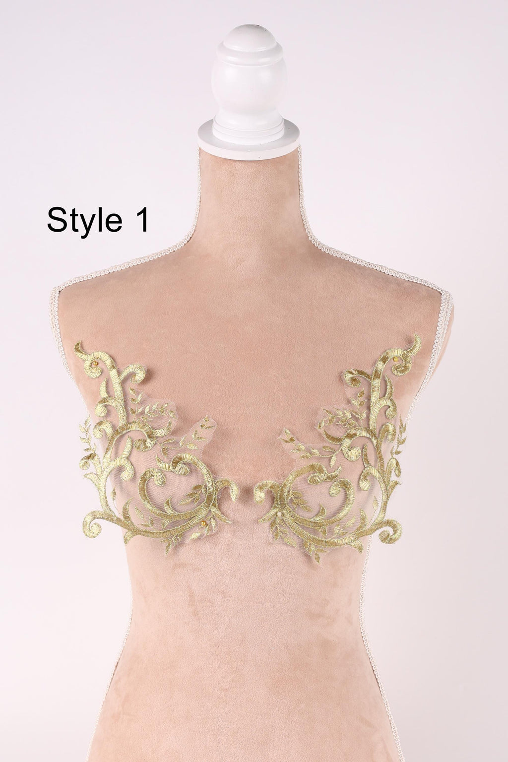 A mannequin with a white head and a beige body, wearing a bra with gold embroidered floral patterns.