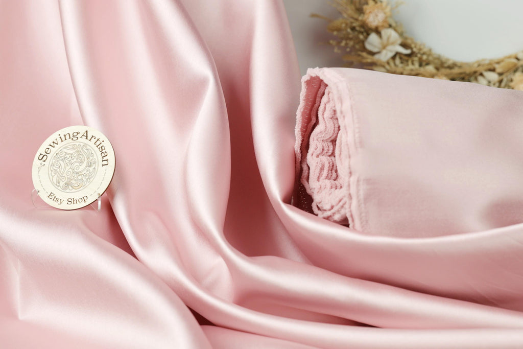 a pink satin fabric with a small white sewing artisan badge placed on it.