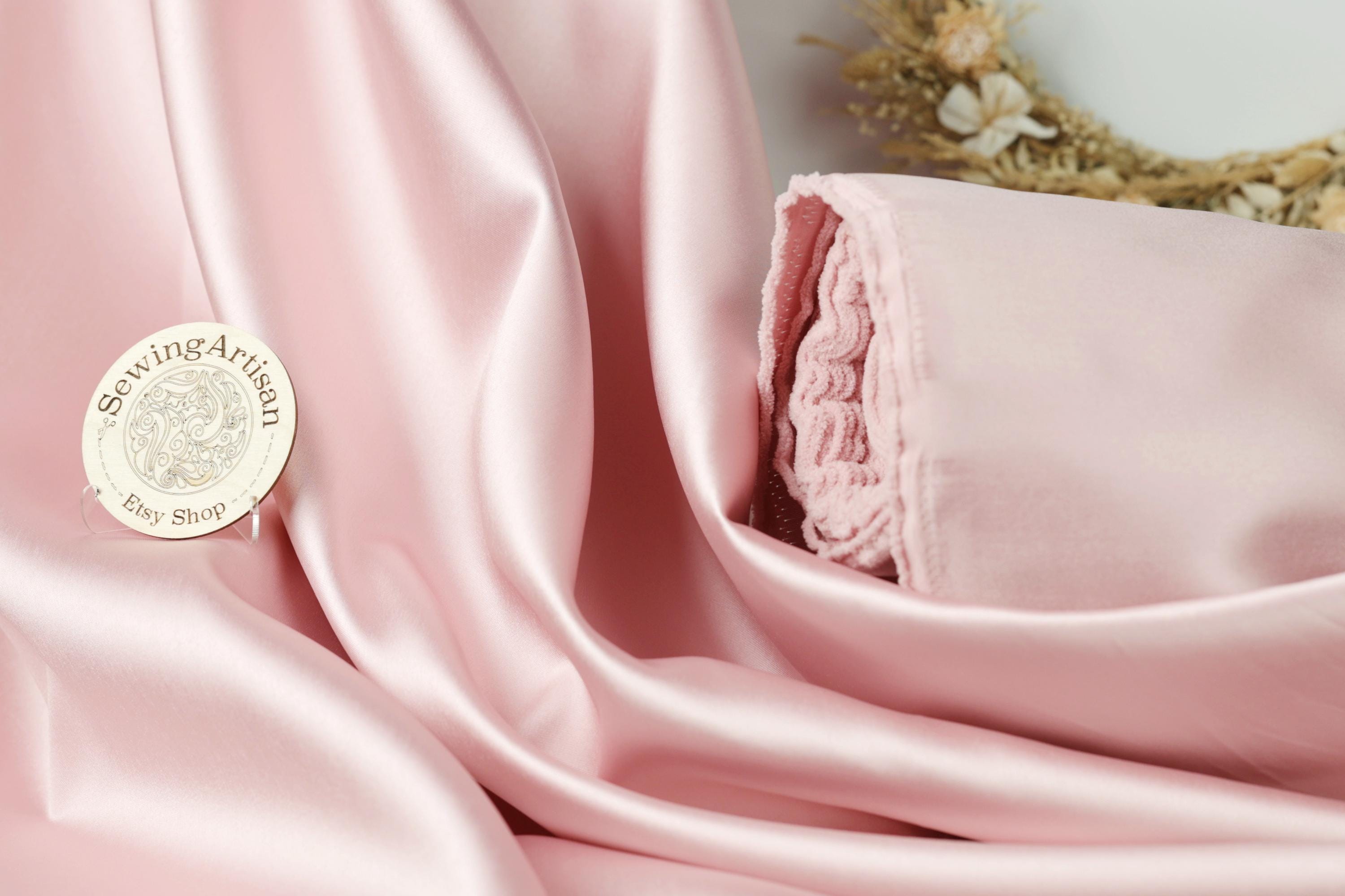 a pink satin fabric with a small white sewing artisan badge placed on it.