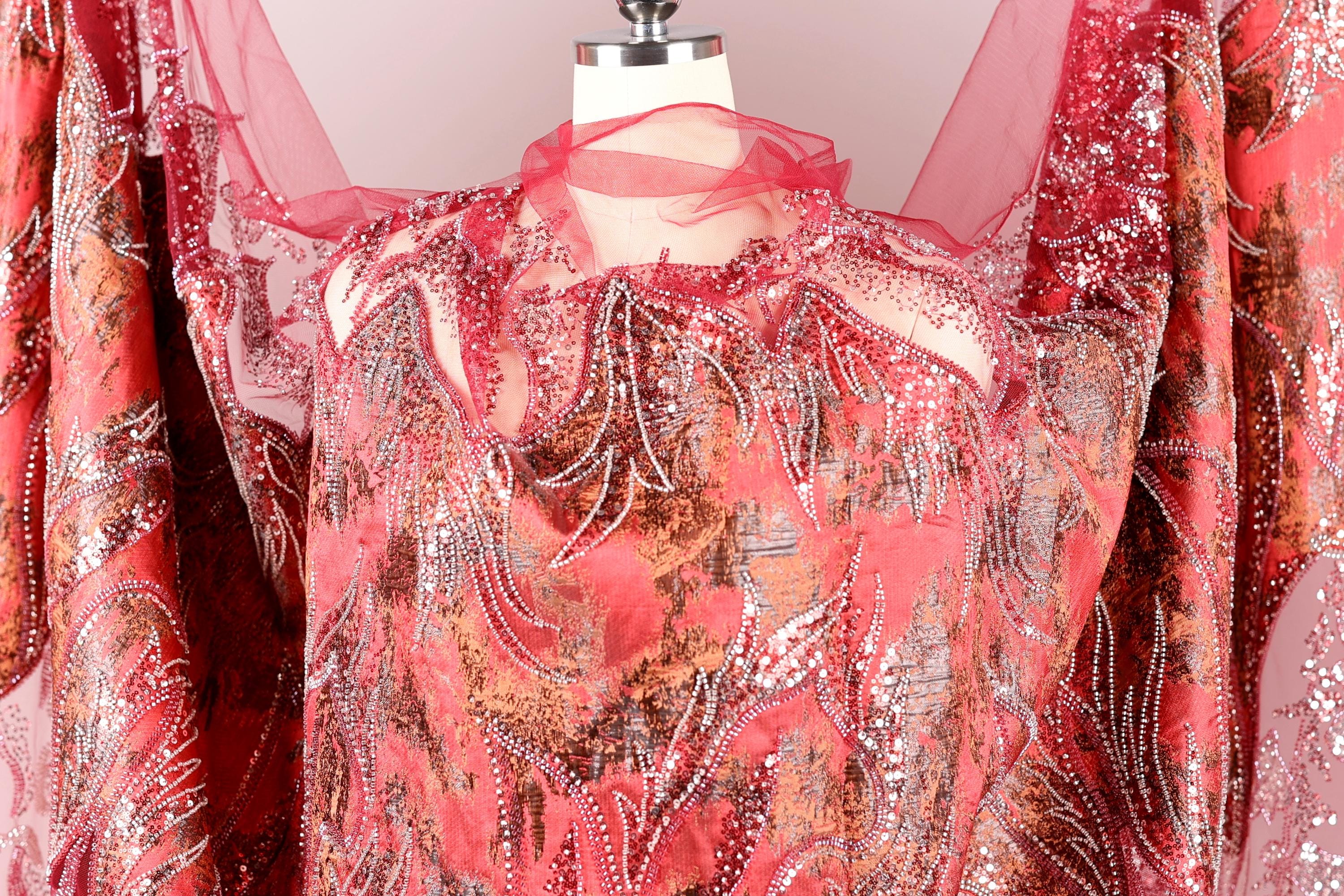 a close-up view of a red and gold patterned fabric, possibly a dress or garment, with intricate designs and embellishments.