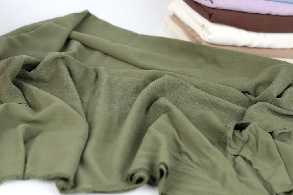 A close-up view of a crumpled green fabric, with a stack of folded fabric visible in the background.