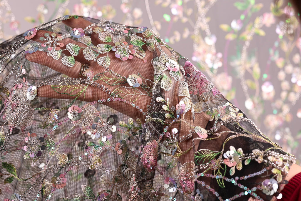A close-up view of a hand holding a delicate, intricately embroidered fabric with a floral pattern.