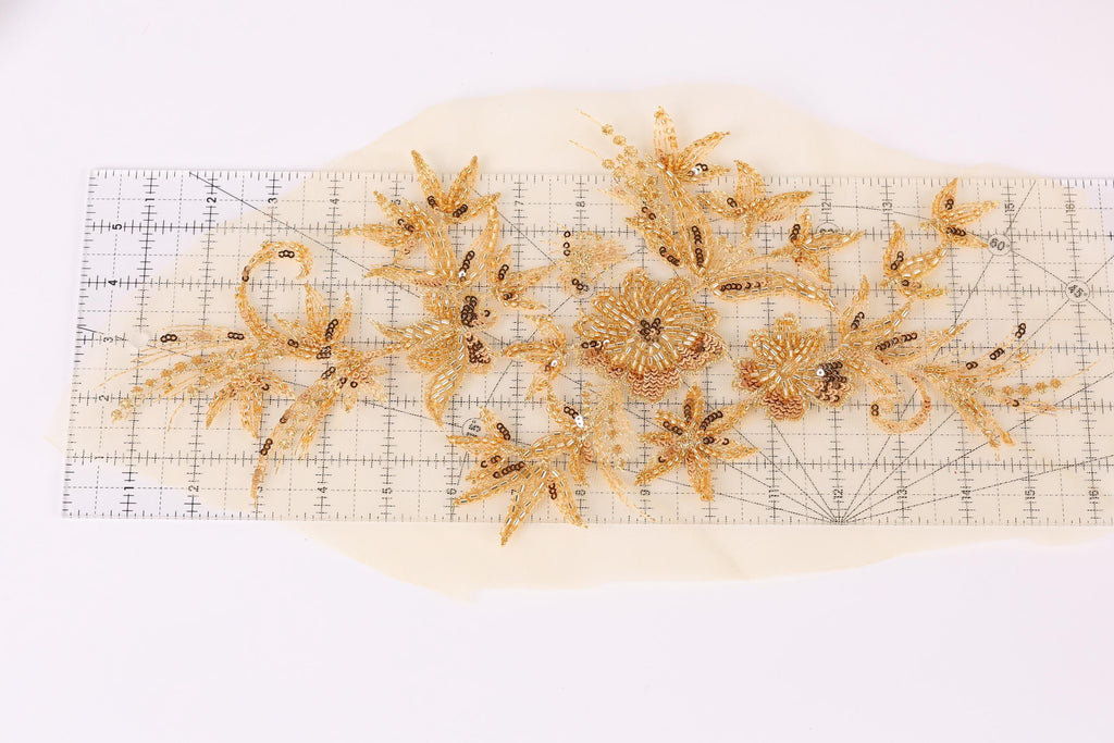 a collection of gold-colored floral designs, including flowers and leaves, arranged on a ruler against a white background.