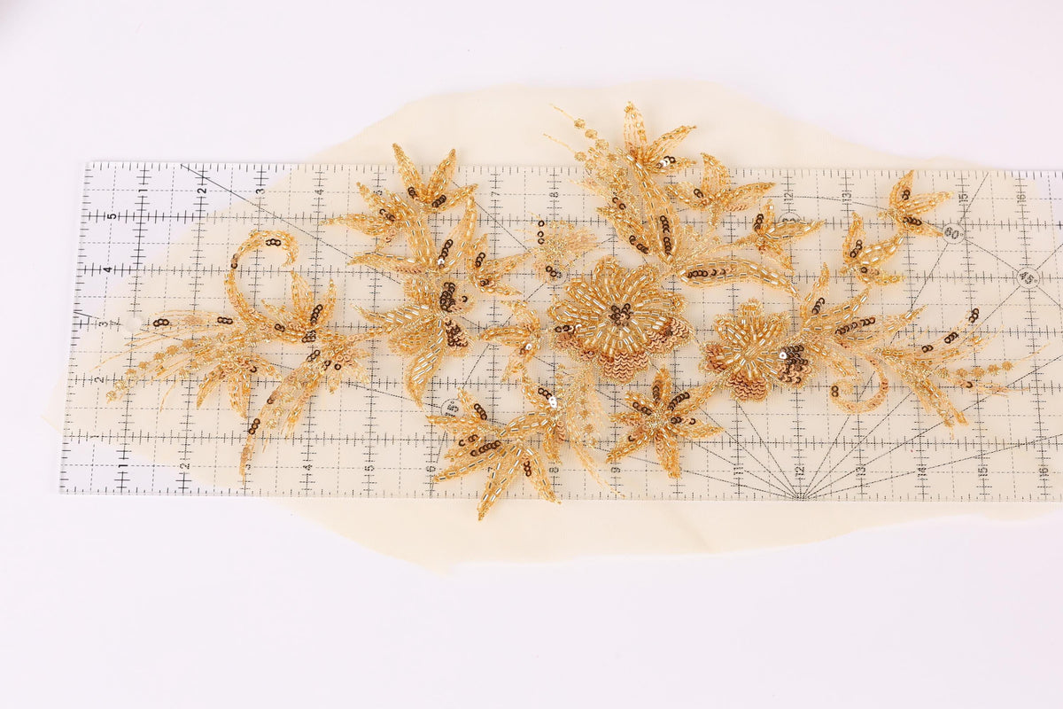 a collection of gold-colored floral designs, including flowers and leaves, arranged on a ruler against a white background.