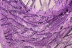 The image is a close-up view of a fabric with a purple and black sequin pattern. The fabric appears to be made of sheer material, with a textured and layered appearance. The image does not contain any discernible text or countable objects, and the focus is on the intricate details of the sequin pattern.