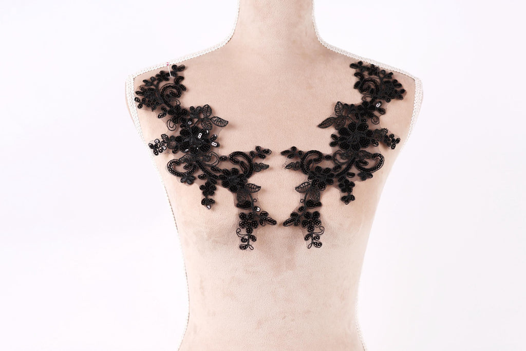 A mannequin wearing a black lace dress with intricate floral patterns.