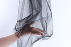 A hand is holding a black, shiny, and textured fabric, which appears to be a sheer or sheer-like material.