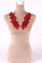 A mannequin wearing a red floral necklace with red flowers and leaves.