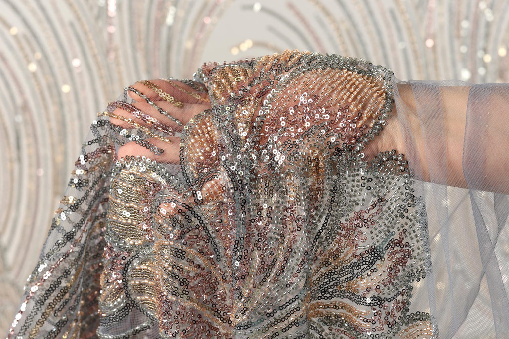 A close-up view of a hand holding a piece of sequined fabric, with the fabric's intricate patterns and shimmering beads visible.