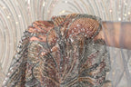 A close-up view of a hand holding a piece of sequined fabric, with the fabric's intricate patterns and shimmering beads visible.