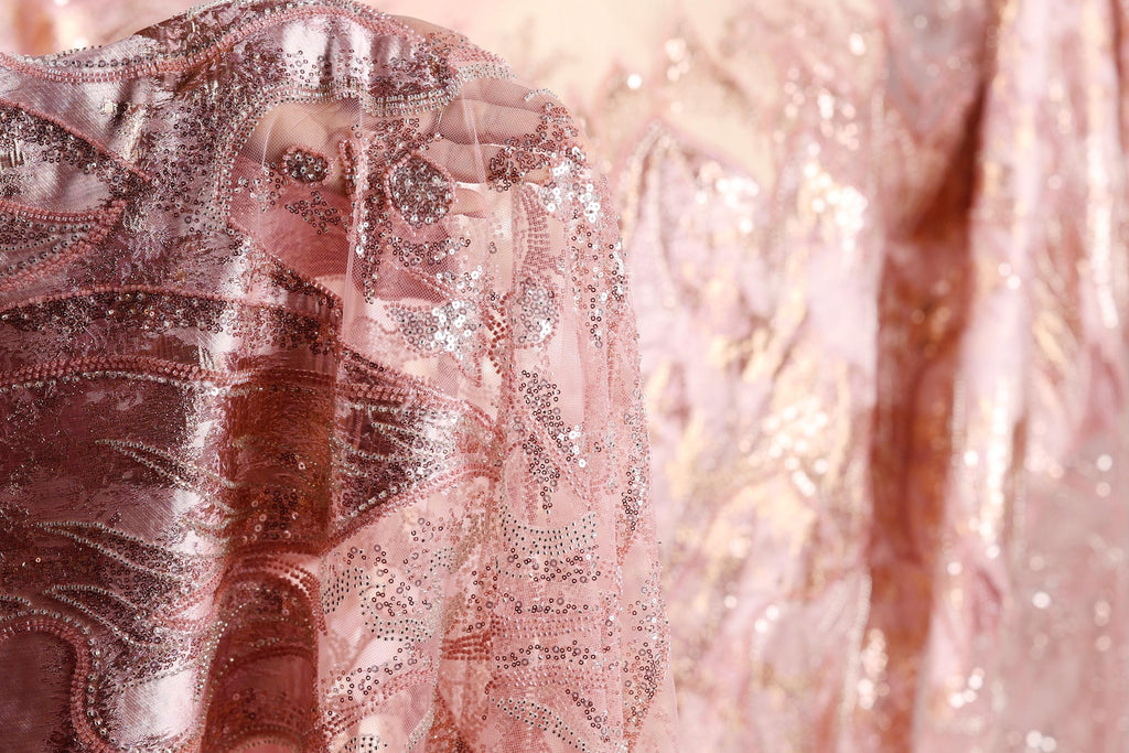A close-up view of a delicate, pink fabric with intricate beading and sequin details, creating a visually striking and elegant appearance.