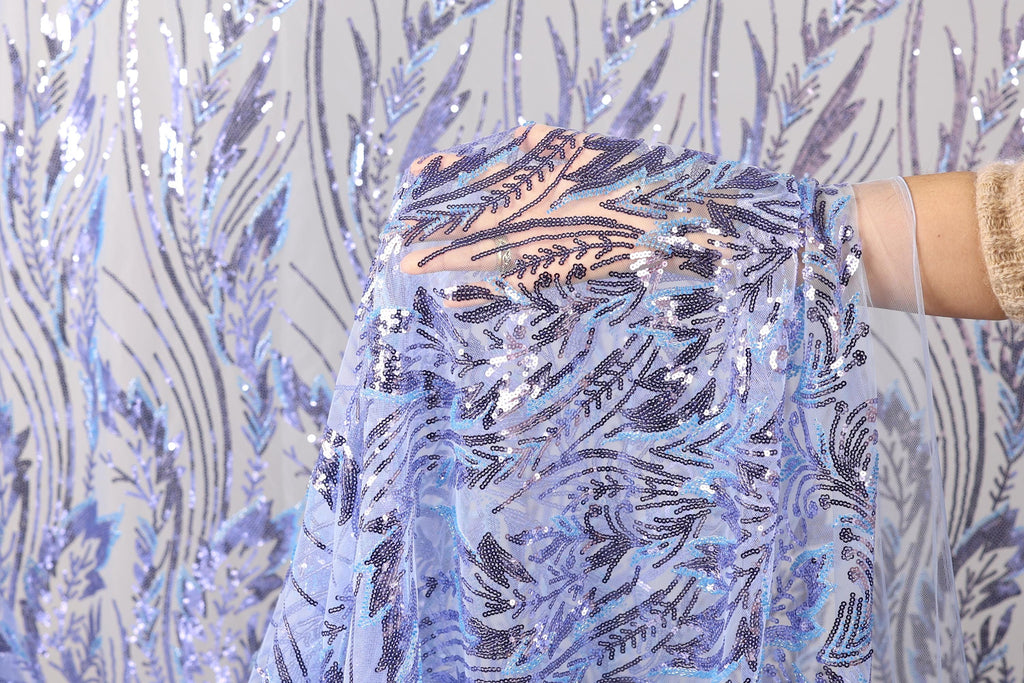A hand is holding up a piece of fabric with a blue and purple floral pattern, against a background of sequin fabric.