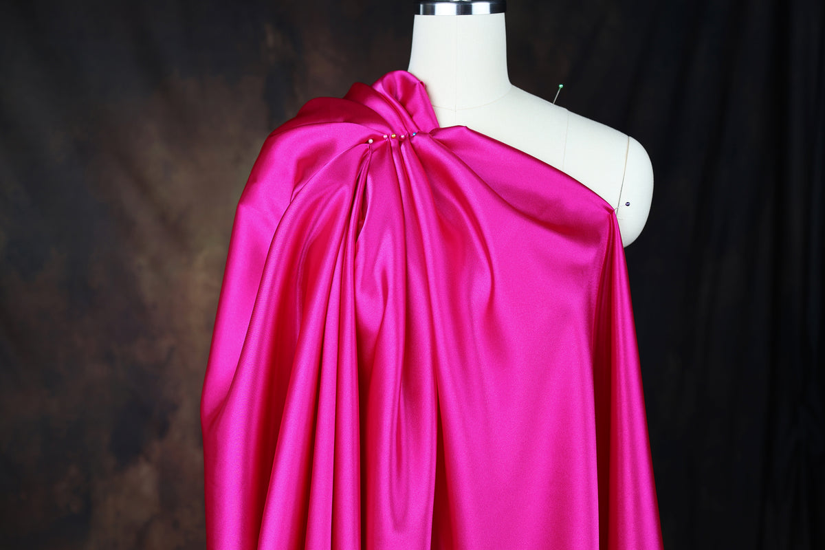 A mannequin wearing a bright pink one-shoulder dress against a dark background.