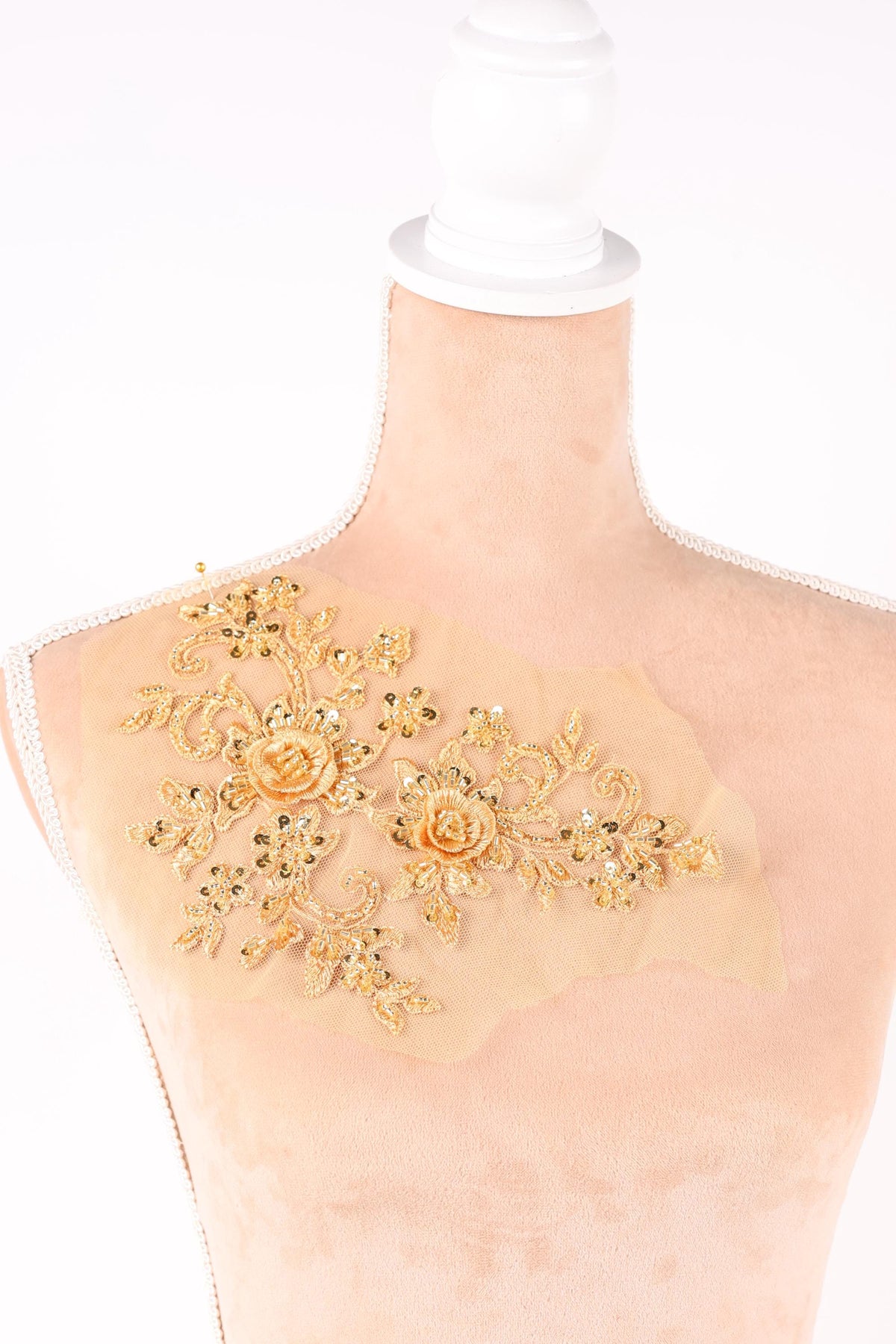 a close-up view of a delicate, beige fabric with a gold floral embroidered design on it.