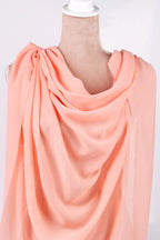 A mannequin wearing a peach-colored draped fabric draped over its shoulders.