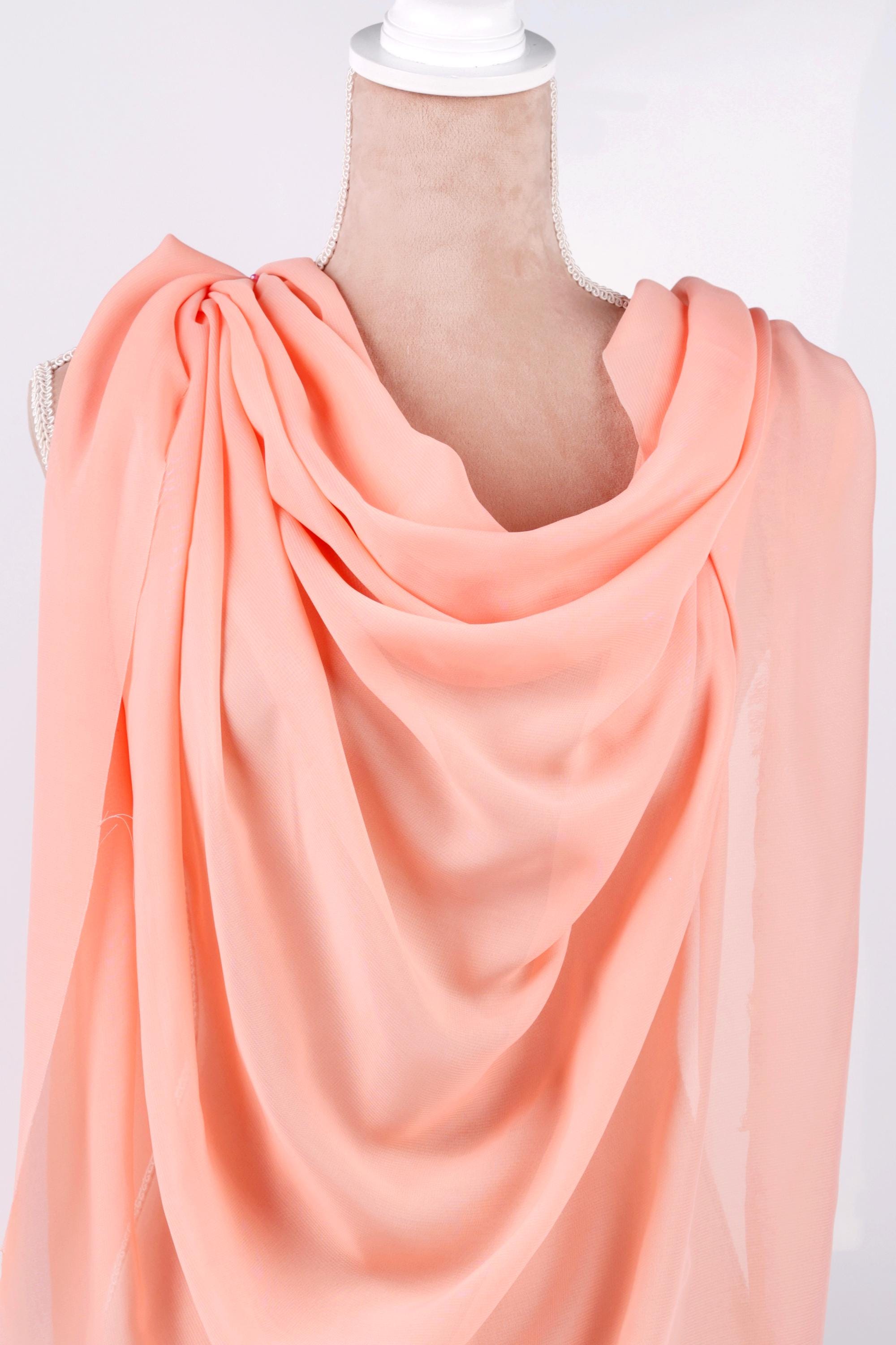 A mannequin wearing a peach-colored draped fabric draped over its shoulders.