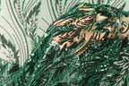 a close-up view of a hand holding a piece of green fabric with a floral pattern made of sequins.