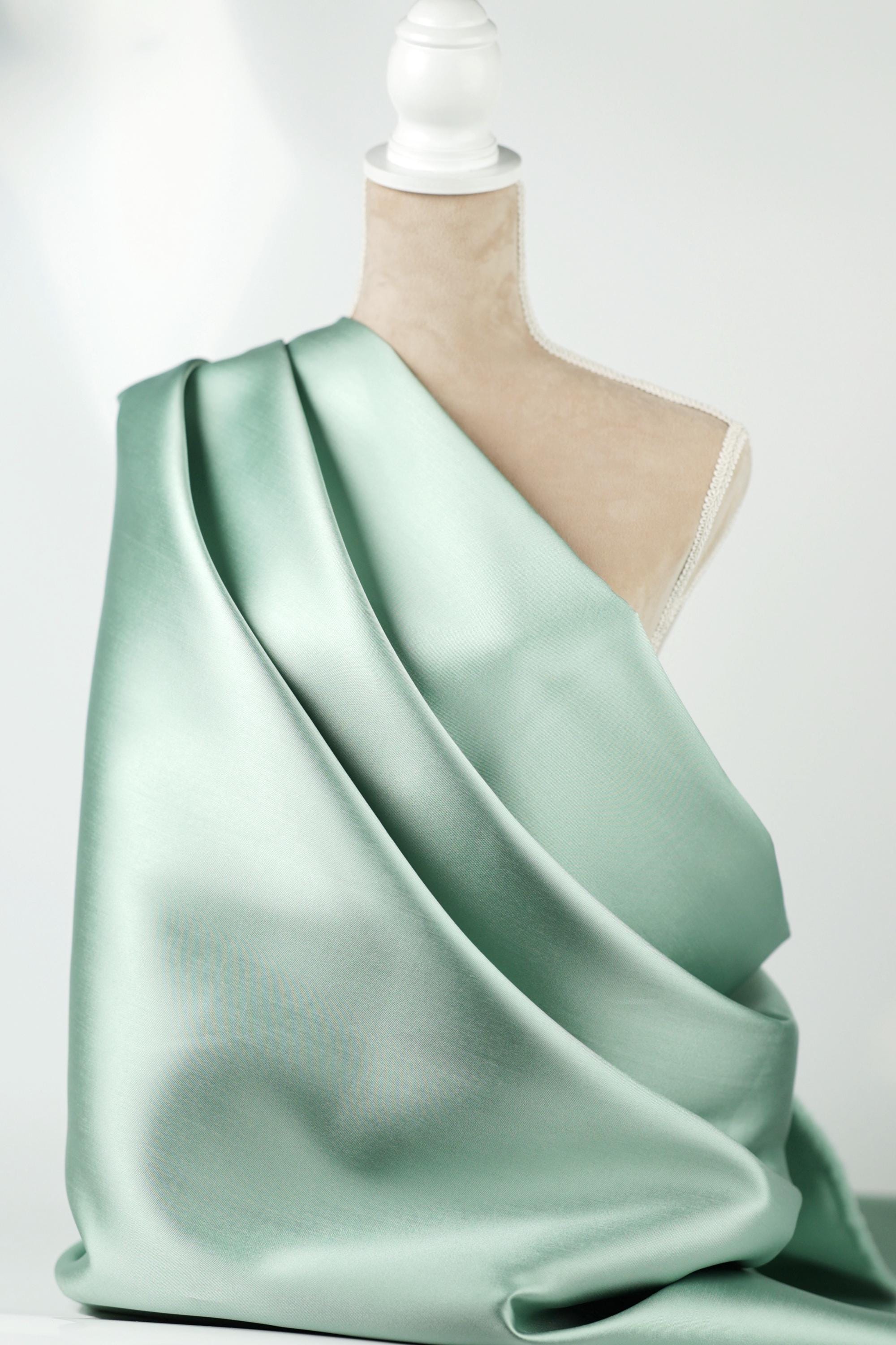 A mannequin is wearing a flowing, mint green satin fabric draped over its body.
