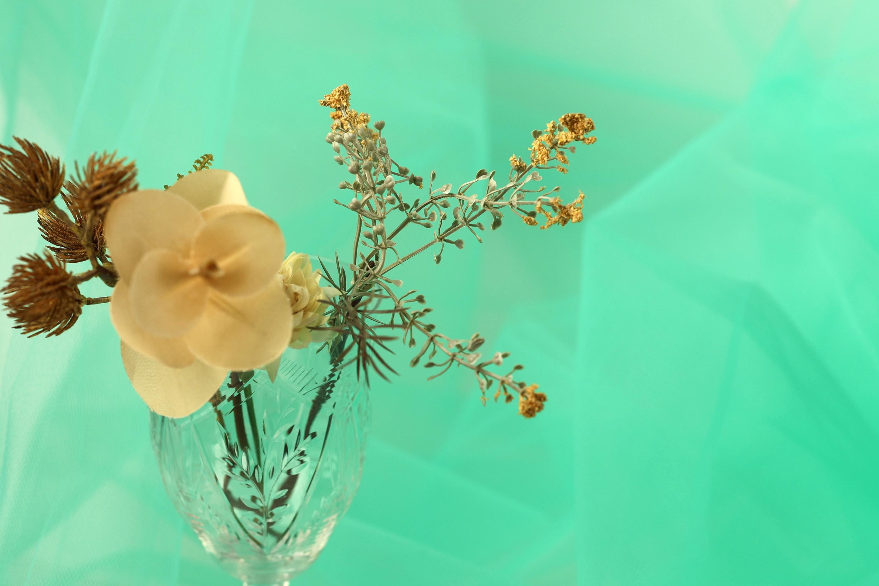 A clear glass vase filled with a variety of flowers and branches sits on a turquoise background.
