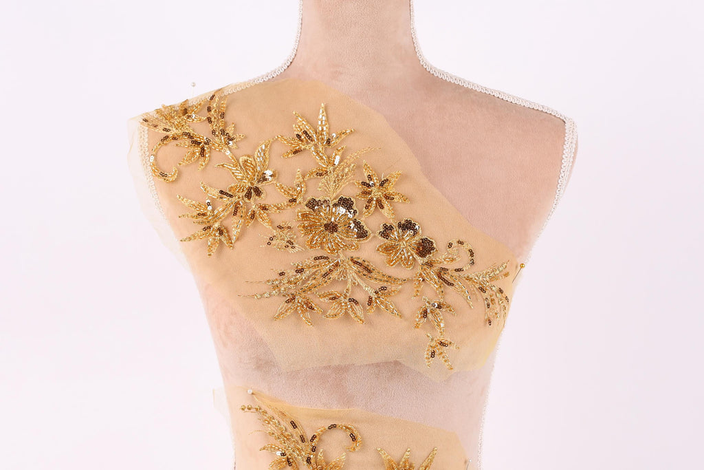 A mannequin with a beige fabric back, adorned with intricate gold embroidery in the shape of flowers and leaves.