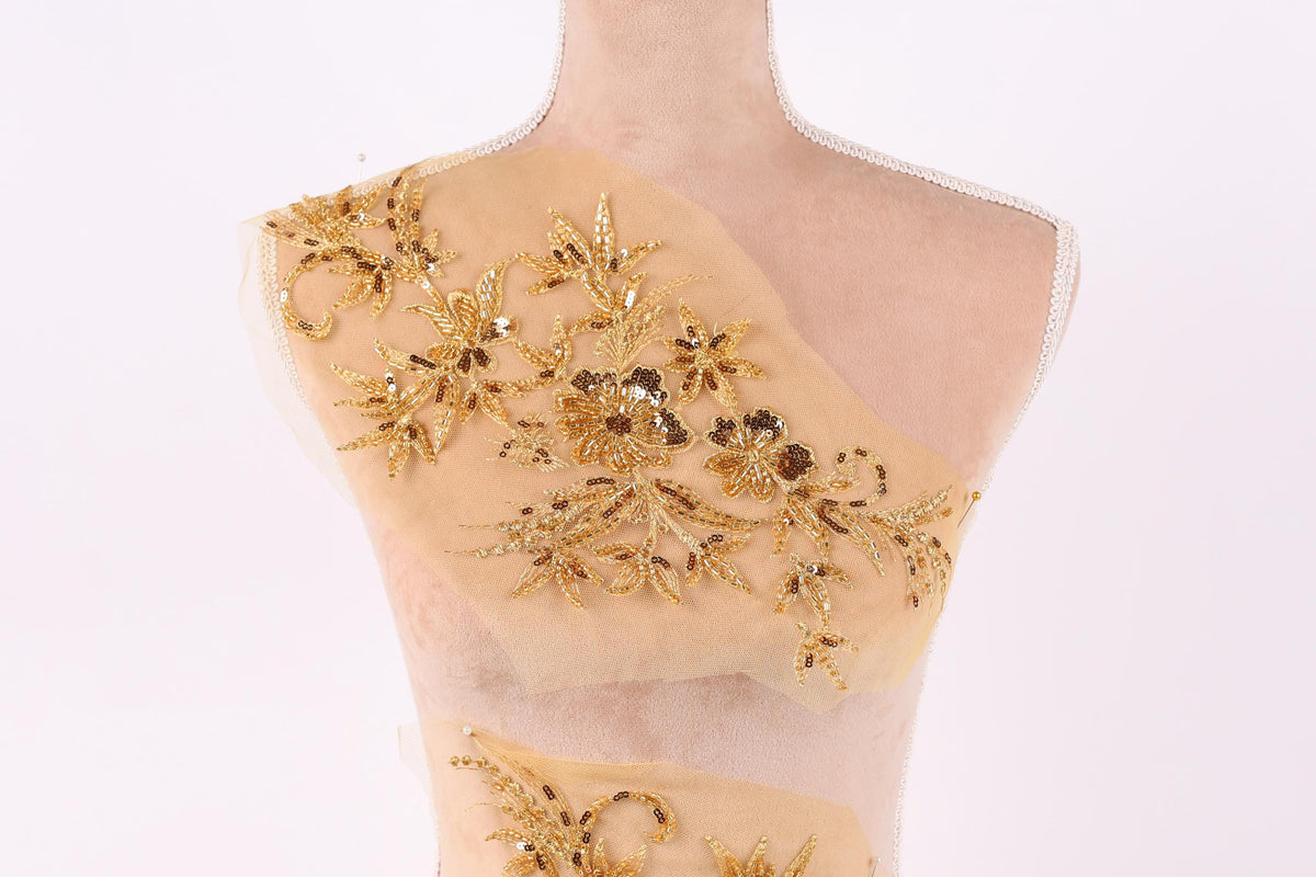 A mannequin with a beige fabric back, adorned with intricate gold embroidery in the shape of flowers and leaves.