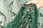 A hand is holding a piece of green sequined fabric with a floral pattern.