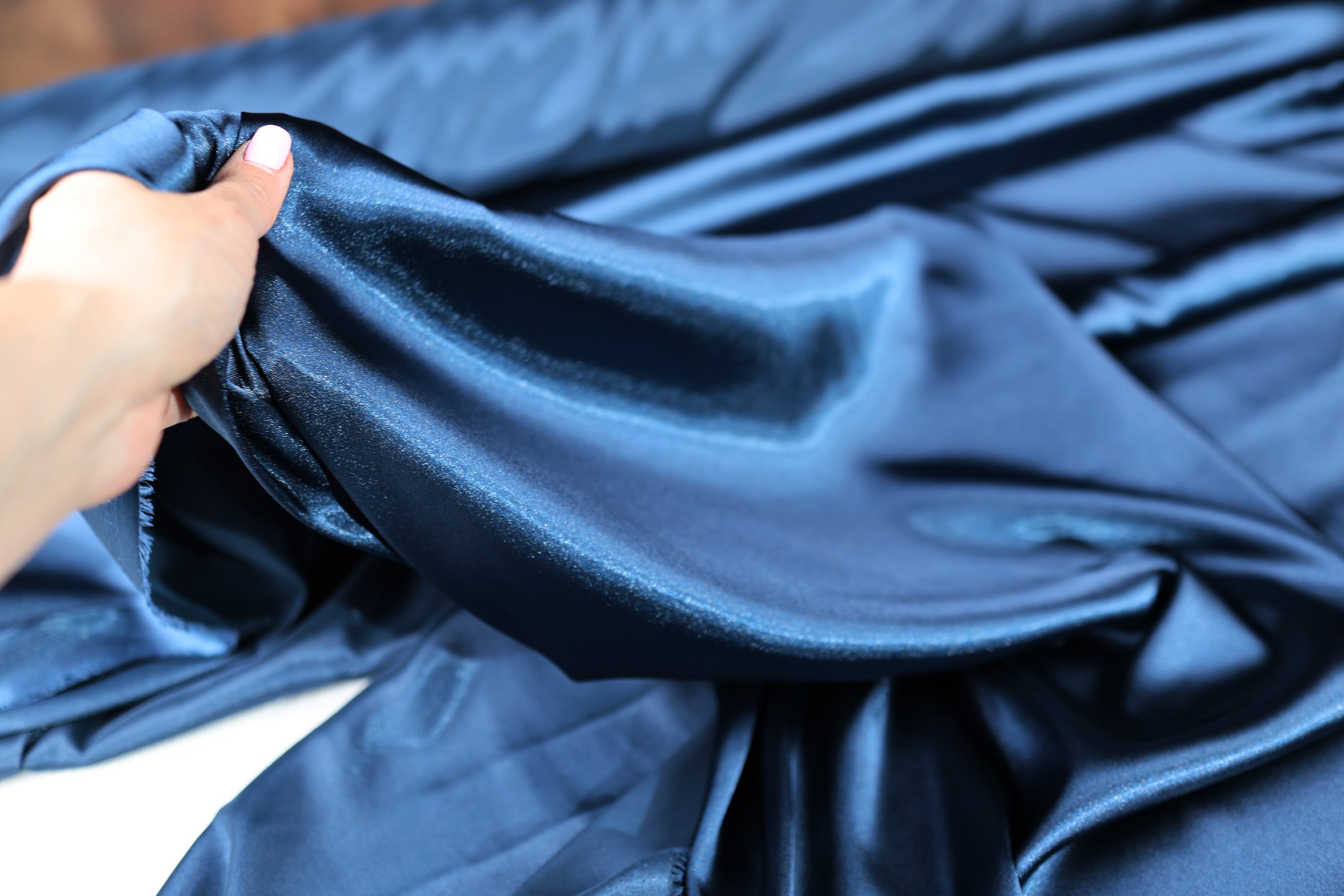 A hand is holding a piece of blue satin fabric, examining its texture and appearance.